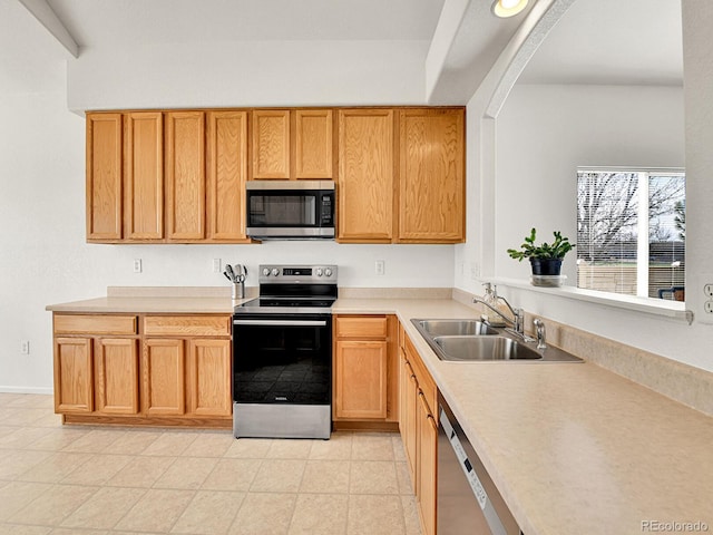 kitchen with light tile patterned floors, a sink, arched walkways, light countertops, and appliances with stainless steel finishes