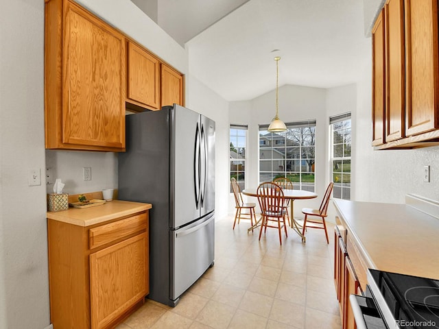kitchen featuring freestanding refrigerator, decorative light fixtures, vaulted ceiling, brown cabinets, and light countertops