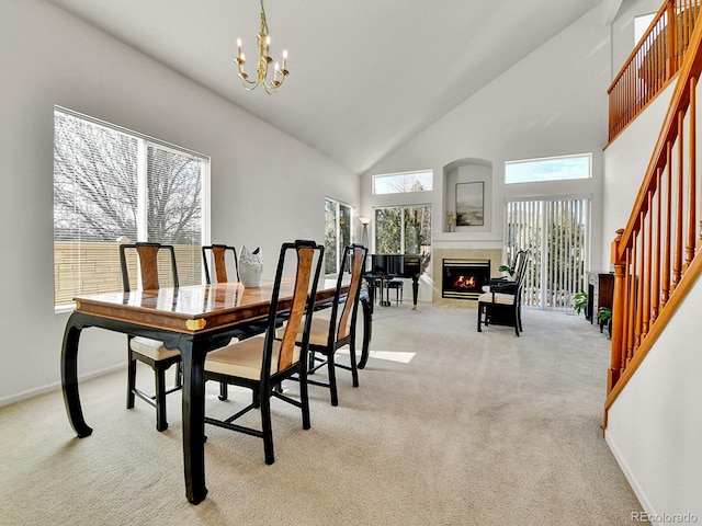 dining room featuring stairs, light colored carpet, high vaulted ceiling, an inviting chandelier, and a tiled fireplace