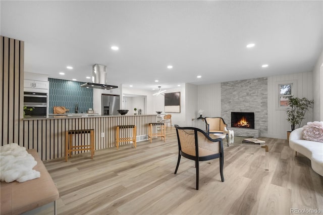 living area featuring light wood finished floors, a stone fireplace, and recessed lighting
