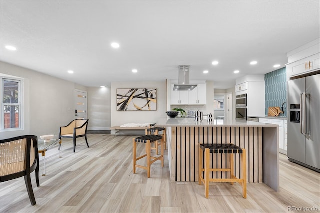 kitchen featuring appliances with stainless steel finishes, a kitchen breakfast bar, light countertops, light wood finished floors, and recessed lighting