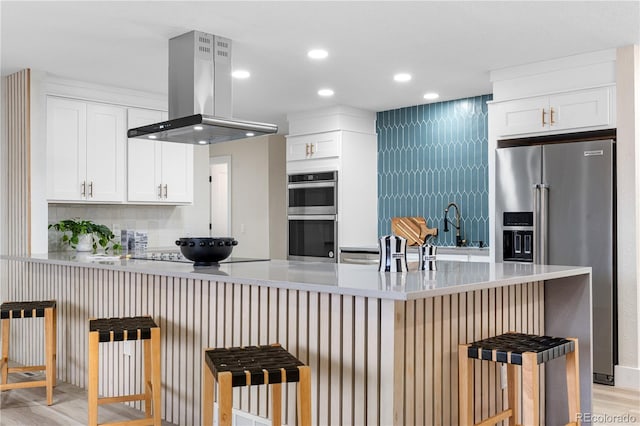 kitchen with stainless steel appliances, island exhaust hood, a peninsula, white cabinets, and light countertops