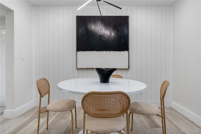 dining room with light wood-style floors, baseboards, and wooden walls
