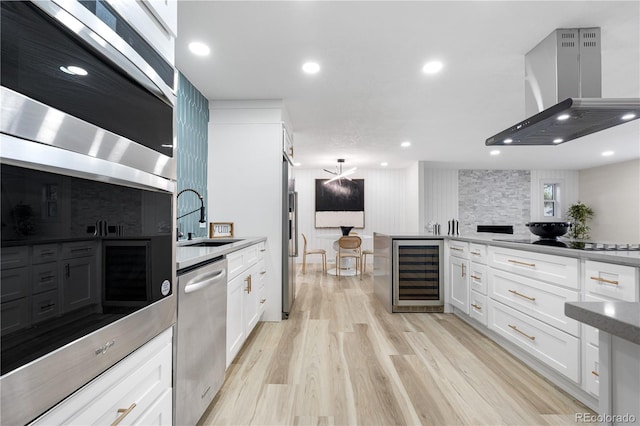 kitchen featuring beverage cooler, a sink, island exhaust hood, appliances with stainless steel finishes, and white cabinetry