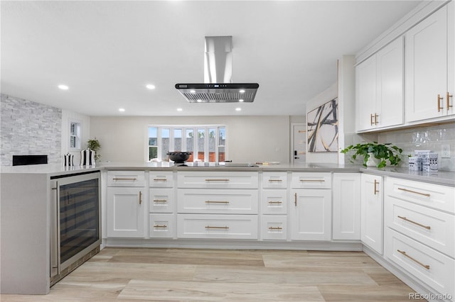 kitchen featuring beverage cooler, island exhaust hood, black electric cooktop, decorative backsplash, and white cabinets