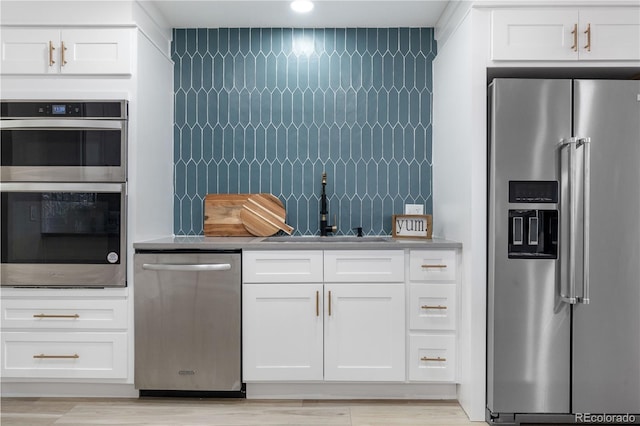 kitchen with stainless steel appliances, a sink, white cabinetry, and tasteful backsplash