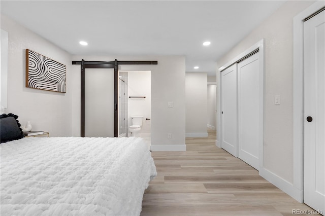 bedroom featuring a barn door, light wood finished floors, recessed lighting, ensuite bathroom, and a closet