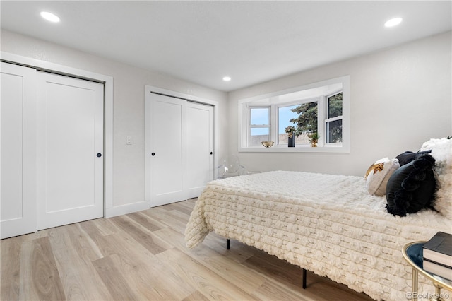 bedroom with two closets, light wood finished floors, and recessed lighting
