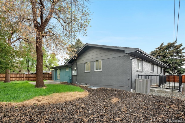 rear view of house with central AC, brick siding, and a fenced backyard