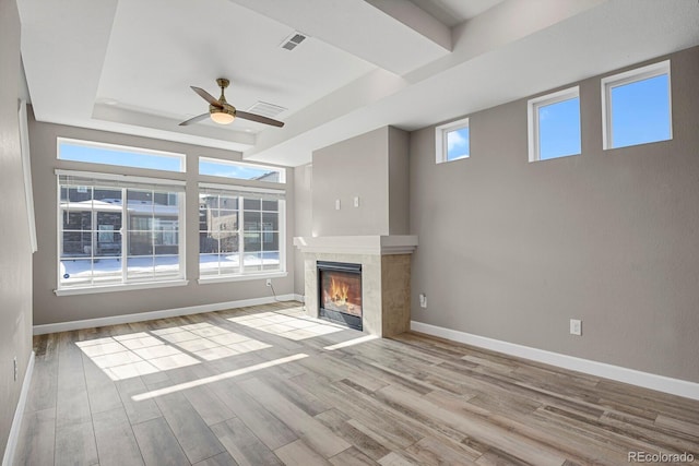 unfurnished living room with a tray ceiling, baseboards, light wood-style flooring, and a tiled fireplace