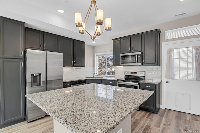 kitchen featuring light stone countertops, light wood-style floors, appliances with stainless steel finishes, a center island, and pendant lighting