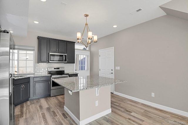 kitchen with stainless steel appliances, a kitchen island, visible vents, hanging light fixtures, and light stone countertops