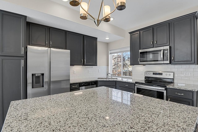 kitchen with stainless steel appliances, a sink, dark cabinetry, decorative backsplash, and pendant lighting