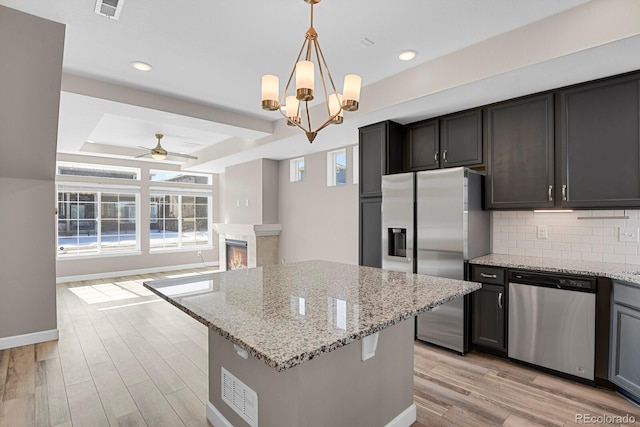 kitchen featuring a tray ceiling, hanging light fixtures, appliances with stainless steel finishes, a glass covered fireplace, and light stone countertops