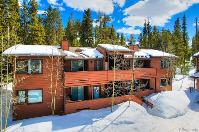 snow covered back of property featuring a chimney