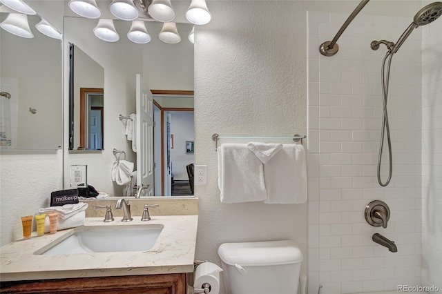 full bath with vanity, toilet, a textured wall, and tiled shower