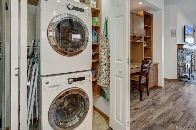 laundry room with baseboards, laundry area, stacked washer / drying machine, and wood finished floors