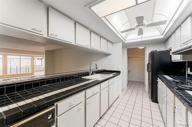 kitchen featuring sink, ceiling fan, light tile patterned floors, tile counters, and white cabinetry