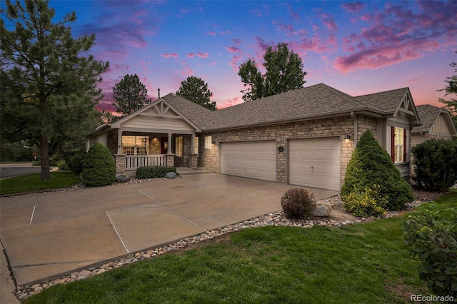 view of front of home with a porch, an attached garage, driveway, stone siding, and a yard