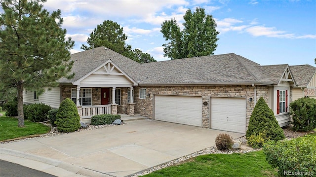 view of front of home with a garage, a porch, driveway, stone siding, and roof with shingles