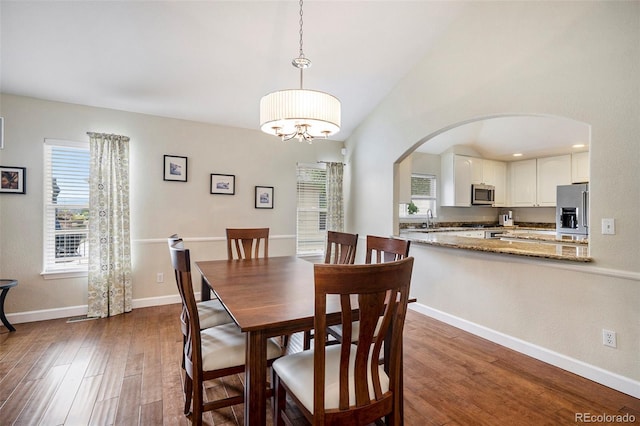 dining room with plenty of natural light, arched walkways, dark wood-style floors, and vaulted ceiling
