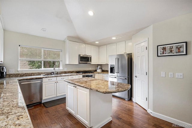 kitchen with appliances with stainless steel finishes, a sink, light stone countertops, dark wood-type flooring, and white cabinetry