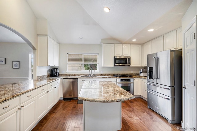 kitchen with stainless steel appliances, arched walkways, light stone countertops, a sink, and vaulted ceiling