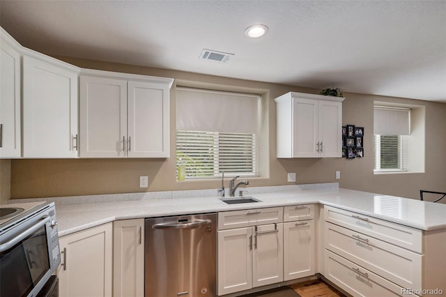 kitchen featuring stainless steel appliances, a sink, a peninsula, light countertops, and white cabinetry