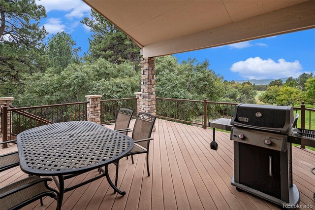 wooden terrace with a grill, outdoor dining space, and view of wooded area