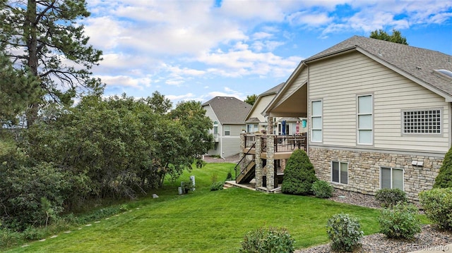back of property with stone siding, a deck, a yard, stairway, and roof with shingles