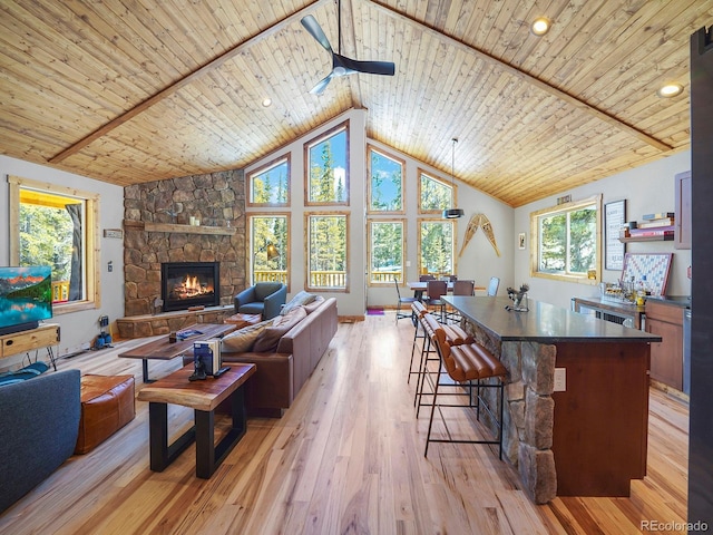 living room featuring wooden ceiling, high vaulted ceiling, a stone fireplace, ceiling fan, and light hardwood / wood-style floors