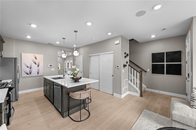 kitchen featuring an island with sink, light wood-type flooring, hanging light fixtures, sink, and appliances with stainless steel finishes