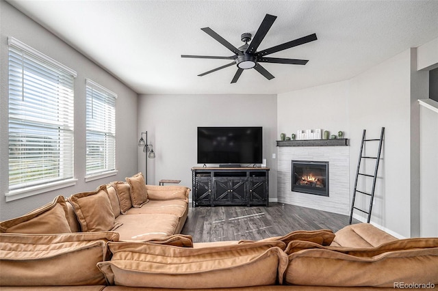 living room featuring ceiling fan, a stone fireplace, a textured ceiling, and dark hardwood / wood-style flooring