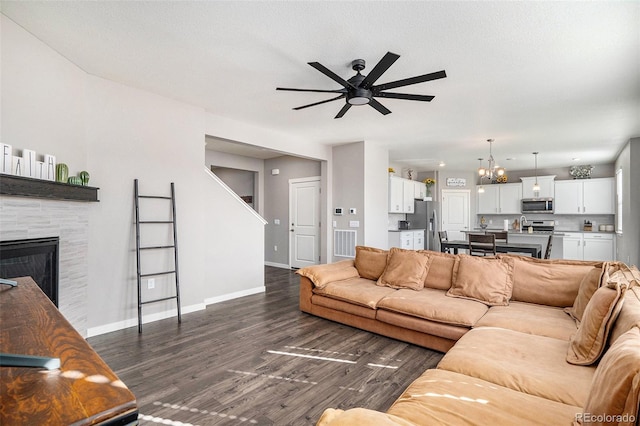 living room featuring dark wood-type flooring, a textured ceiling, a tiled fireplace, and ceiling fan with notable chandelier