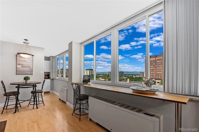 kitchen featuring radiator, baseboards, light wood-style flooring, a view of city, and decorative light fixtures