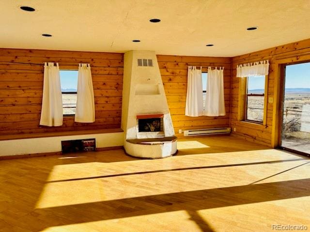 unfurnished room with light hardwood / wood-style floors, a baseboard heating unit, wood walls, and a fireplace