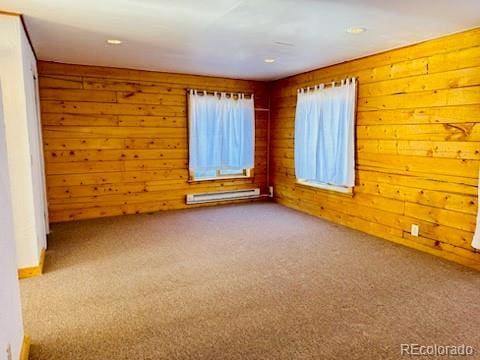 empty room featuring carpet flooring, wood walls, and baseboard heating