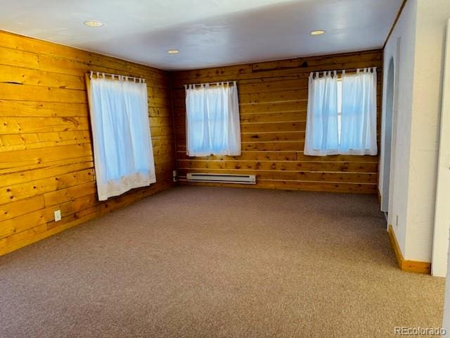 carpeted empty room featuring wooden walls and a baseboard heating unit