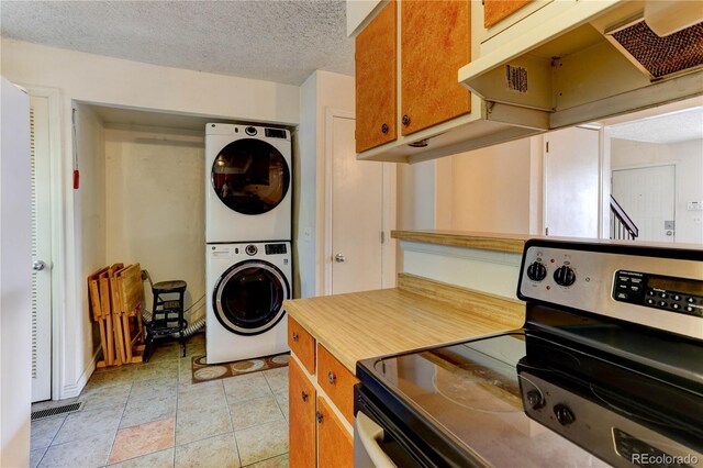 8144 Washington St Unit 192, Denver, CO 80229 - kitchen featuring stainless steel electric range oven, estacked washer and dryer, under cabinet range hood, brown cabinets, and a textured ceiling