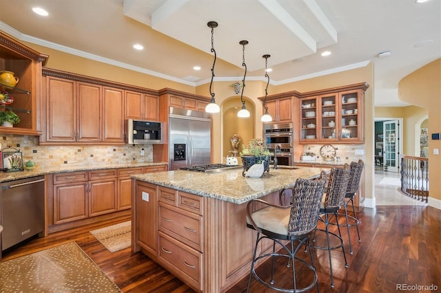 5335 E 2nd Ave, Denver, CO 80220 - kitchen featuring stainless steel appliances, dark wood-style floors, a center island with sink, brown cabinetry, and light stone countertops