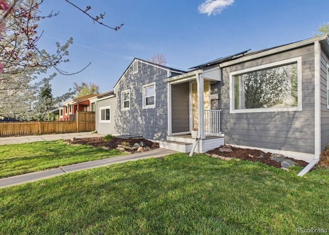 view of front of home featuring a front lawn, fence, and roof mounted solar panels