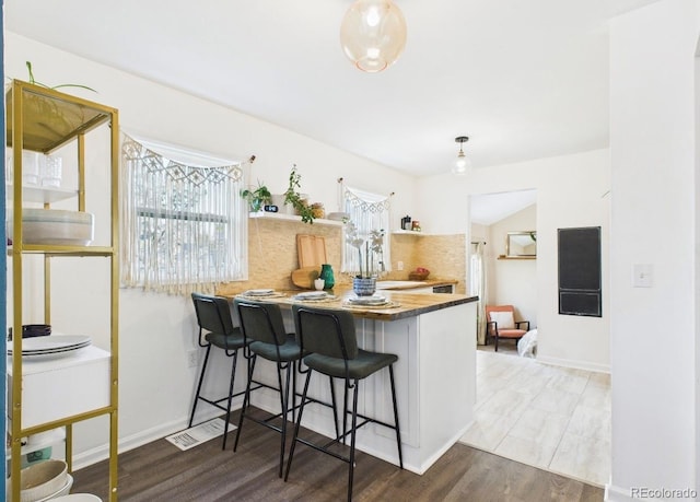 kitchen with a peninsula, open shelves, wood finished floors, a breakfast bar area, and baseboards