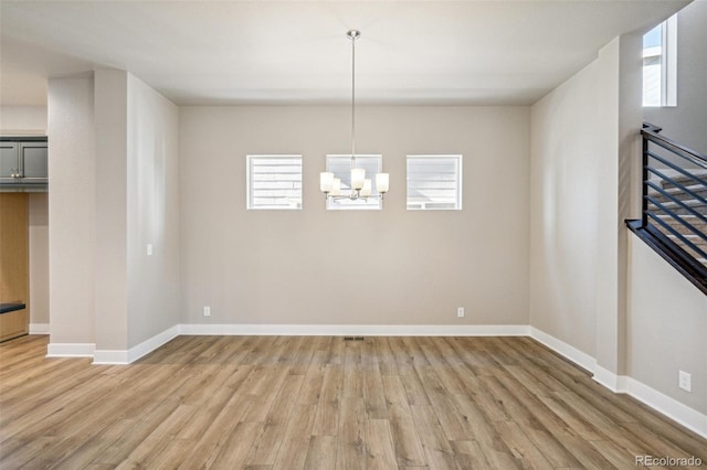 unfurnished room with a wealth of natural light, a notable chandelier, and light wood-type flooring