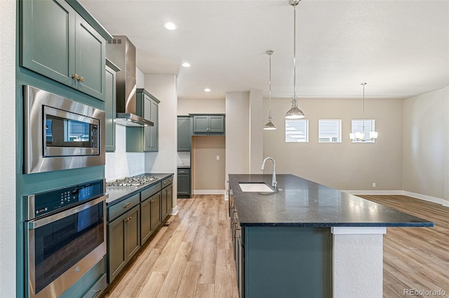 kitchen featuring sink, light hardwood / wood-style floors, decorative light fixtures, a center island with sink, and appliances with stainless steel finishes