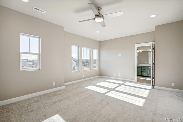 unfurnished bedroom featuring ceiling fan, light carpet, connected bathroom, and multiple windows