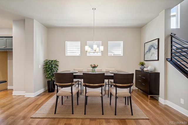 dining area featuring light wood-type flooring, a notable chandelier, stairway, and baseboards