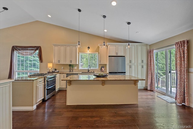 9406 Troon Village Way, Lone Tree, CO 80124 - kitchen featuring appliances with stainless steel finishes, lofted ceiling, dark wood-style floors, cream cabinetry, and light stone countertops