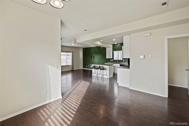 unfurnished living room with dark wood-style floors, visible vents, baseboards, and a sink