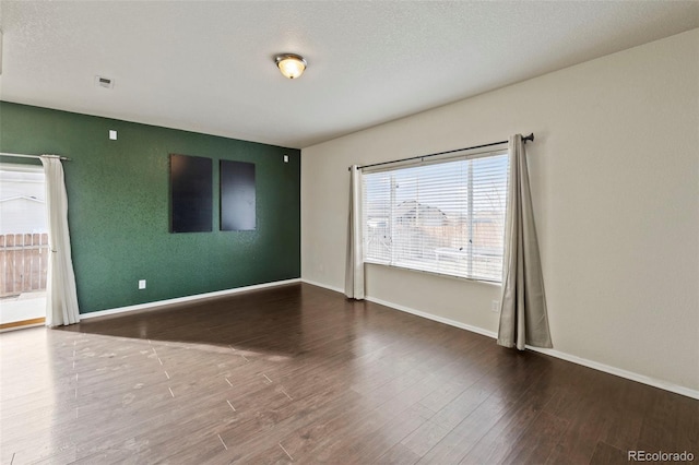 empty room with dark wood-style flooring, visible vents, a textured ceiling, and baseboards