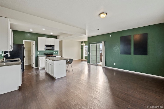 kitchen featuring a center island, dark wood-style flooring, dark countertops, white cabinetry, and black appliances